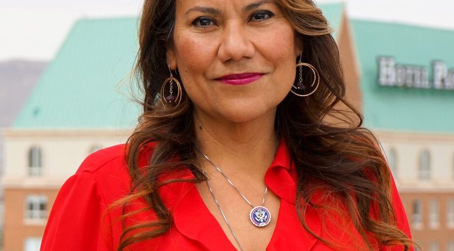Veronica Escobar is pictured standing outdoors in a red dress with mountains in the background.