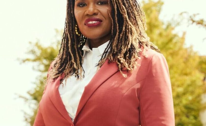 This is an image of Cori Bush, candidate for Missouri's 1st Congressional District. She is pictured in a red suit on a street in front of the St. Louis arch.