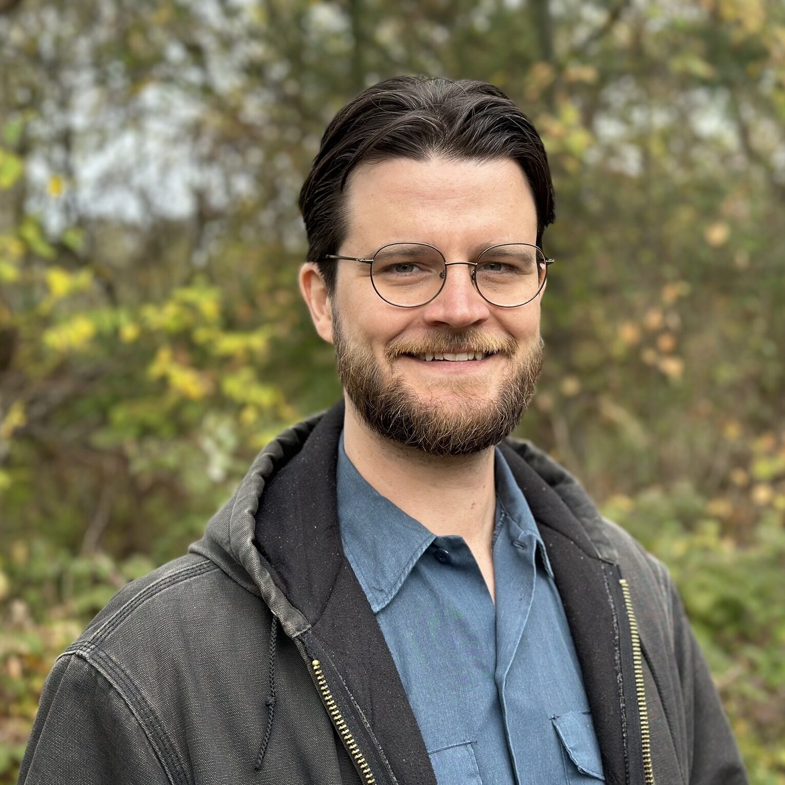This is an image of William Lawrence, candidate for Michigan's 7th Congressional District. He is pictured in a blue shirt and gray hoodie in front of a forest.