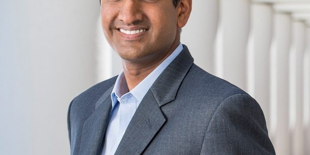 This is an image of Ro Khanna, candidate for California's 17th Congressional District. He is pictured in a gray suit standing in front of white pillars.