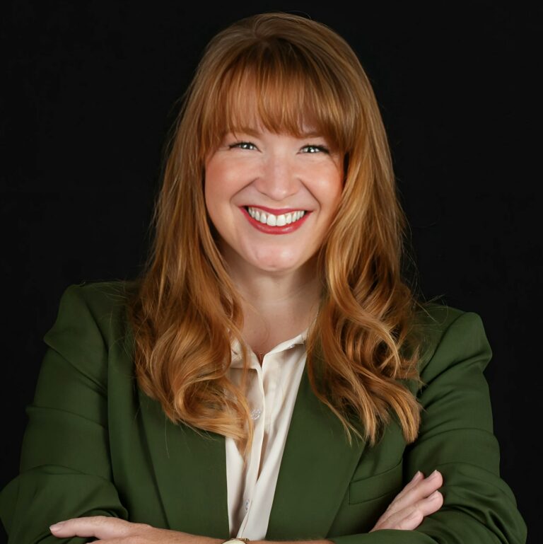 This is an image of Lindsay James, candidate for Iowa's 2nd Congressional District. She is pictured in a green suit with a white shirt in front of a black background.